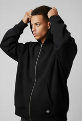 Male model wearing black hoodie with front zipper, adjusting hood in side view