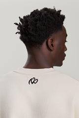 Back view of NV Loose Sweatshirt in beige with black logo detail below neckline