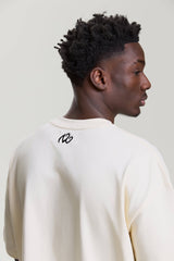 Back view of beige NV Loose T-Shirt showing small black logo below the neckline by Turn Envy To Love