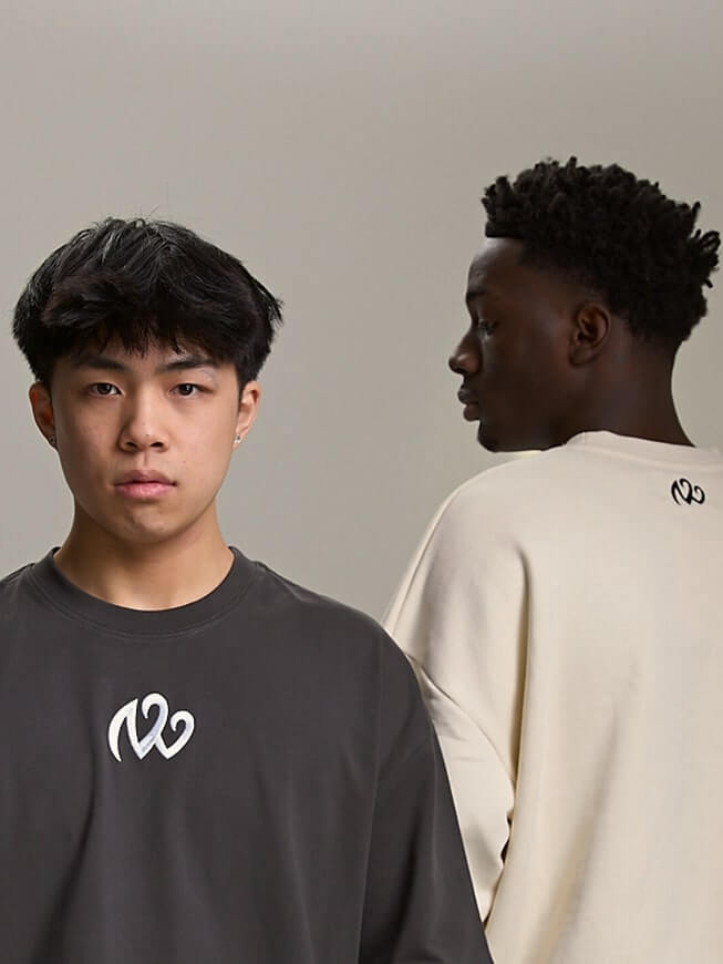 Two models in charcoal and cream crewneck sweatshirts, front chest logo and back neck logo, minimalist studio.