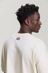 Back view of beige NV Loose T-Shirt showing small black logo below the neckline by Turn Envy To Love