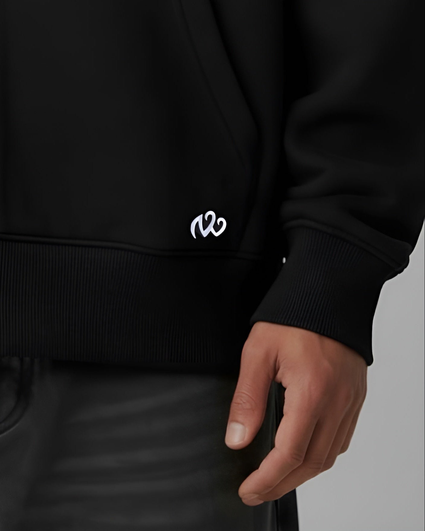 Close-up of black hoodie front hem with small white embroidered logo